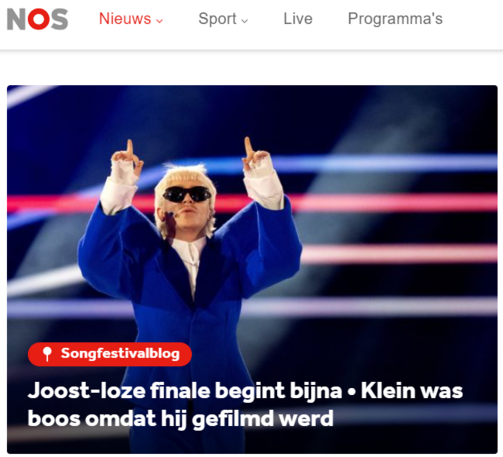 Screenshot van de website NOS, met het gedeelte van het songfestivalblog. Op de achtergrond een foto van Joost Klein tijdens een optreden, handen in de lucht met opgetoken wijsvingers.

Koptekst: 
"Joost-loze finale begint bijna - Klein was boos omdat hij gefilmd werd." 

