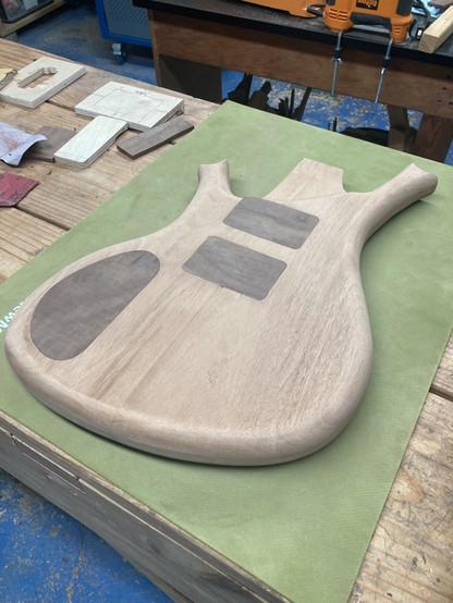 A baritone guitar body in progress sits face down on a workbench, atop a green rubber mat.
