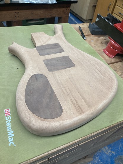 A baritone guitar body in progress sits face down on a workbench, atop a green rubber mat.
