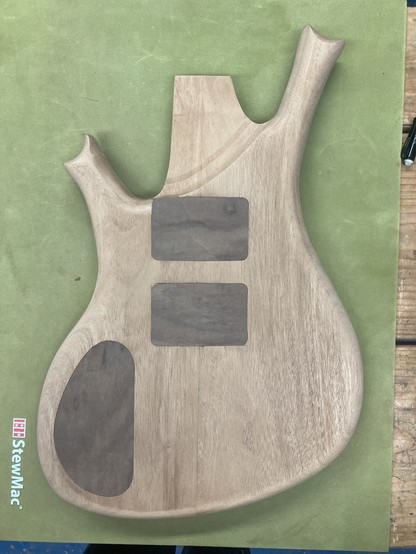A baritone guitar body in progress sits face down on a workbench, atop a green rubber mat.