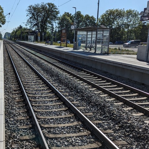 Blick die Schienen entlang in die Ferne an einem zweigleisigen Bahnhof. Ein leeres Wartehäuschen ist sichtbar, die S-Bahn aber noch nicht.