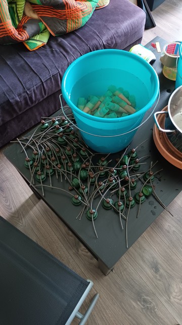 Ein Eimer mit Wasser und Tonkegeln. Daneben verschlusskappen mit dünnen Schläuchen.