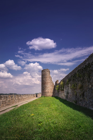 One hot summer day in July I visited Smederevo, a city in the heart of Serbia located right on the bank of the Danube. It is a beautiful city with many cultural sights and a rich historical heritage. One thing that certainly attracts the attention of visitors is the old medieval fortress.
This is a view of the fortified defensive walls and the old partially damaged tower between the walls. It was a very sunny day and I took this picture in the early afternoon, so the lighting was not ideal, but I couldn't wait for the better conditions because I had to go.

One of the main sights of Smederevo is the old medieval fortress from the 15th century, Smederevo Fortress or Jerina town built by Serbian despot Djuradj Brankovic and his wife Jerina in just a few years, which was very fast at the time, so many builders died from exhaustion. People were looking for the culprit, and the wife of the Serbian despot Đurađ Branković - Jerina (Irena Kantakouzene) was blamed for that. It was called "Cursed Jerina" and that name has remained to this day. It was built in the period from 1428-1439. With its position at the confluence of the river Jezava and the Danube, it occupies an area of approximately 11 hectares, has the shape of an irregular triangle and consists of two parts - the Big City and the Small Town. It is the last major creation of a Serbian military building and one of the largest fortifications in Southeast Europe. 

One July day in Smederevo, Serbia.
