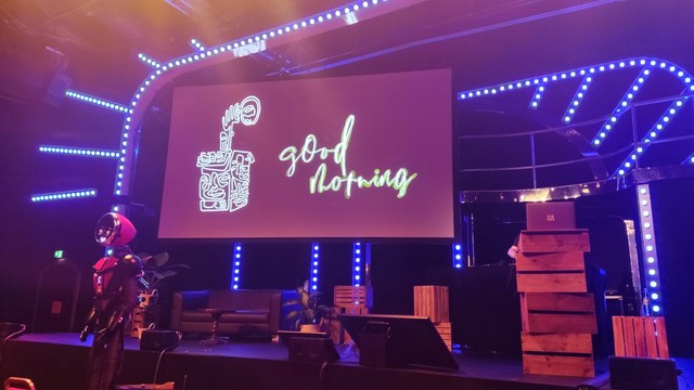 Bühne der beyond tellerrand, ein Roboter im Vordergrund, auf einer großen Leinwand "good morning" 