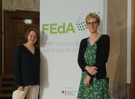 zwei Forscherinnen vor einem Banner mit FEdA-Logo
