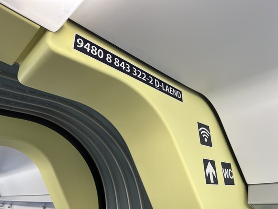 Foto aus dem Inneren eines von der baden-württembergischen SWEG betriebenen Zuges, das auf pastellelgelb diverse Aufkleber zeigt. Auch eine lange Seriennummer ist aufgeklebt. Diese endet mit den Buchstaben LAEND.