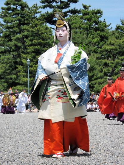 A female attendant parades at the Aoi Matsuri. At her shoulder is a sprig of wild ginger. The plant was believed to be a protective charm, and gives its name to the festival.