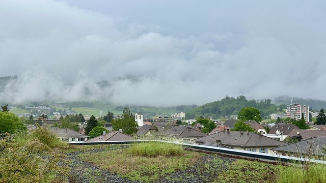 Die grüne/bewachsene Dachterrasse, dahinter die Dächer Ostermundigens und dann viele Nebel- und Wolkenfelder unter grauem Himme.