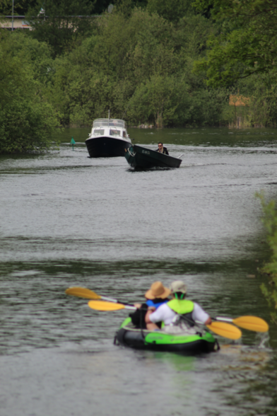 Kanal zwischen zwei Seen. Im Vordergrund zwei Leute in einem Kanu mit Paddel, die aus unserer Perspektive wegfahren. Dahinter zwei Boote, die auf uns zufahren. Am Ufer Bäume.