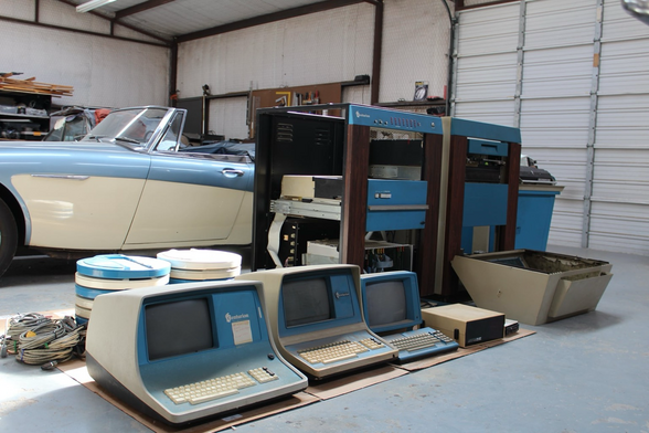 A host of Centurion mini computers and terminals sat in front of a vintage car in a garage. Photo from Usagi Electric's fb page I believe