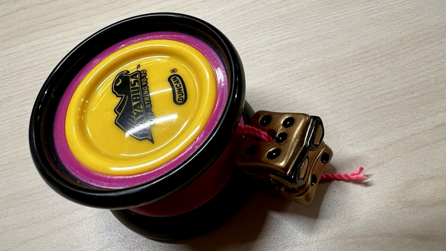 A hot pink, black, and yellow Duncan Hyabusa yo-yo, set up for freehand (5A) play with pink string and a golden die counterweight. 