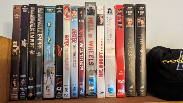 DVD Boxen in einem Regal von links nach rechts:

Staffel 1 "Agent Carter"

Staffel 1 "Jessica Jones"

Staffel 1-2 "Boardwalk Empire"

Staffel 1 "Breaking Bad"

Staffel 1 "Daredevil"

Staffel 1-3 "Dexter"

Staffel 1 "Hell In Wheels"

Staffel 1 "Mr. Robot"

Staffel 1 "Real Humans"

Staffel 2 "Sopranos"

Staffel 1-2 "Tudors"
