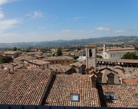 Die Fotografin steht erhöht und schaut über viele rote Dächer und ein paar Kirchtürmen hinweg zu Hügeln und dem leicht bewölkten Himmel.