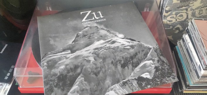 Vinyl record cover, Zu's 2009 record titled 'Carboniferous', lying on top of a Pro-Ject record player. Some CD's and other records visible next to the player.

The cover has a black and white picture of a mountain top, with band name and album title printed above.