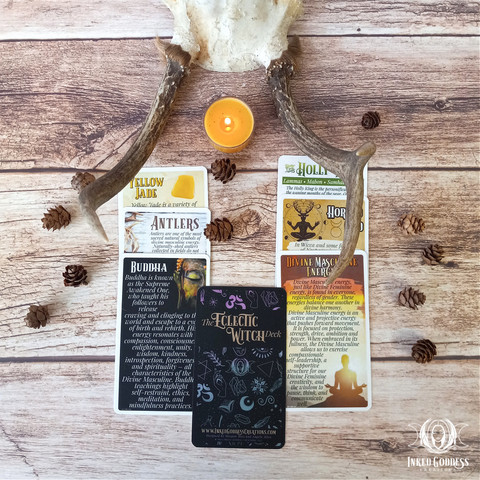 A set of eight cards are arranged on a pale wooden surface. Each card in the "Divine Masculine Expansion Pack for the Eclectic Witch Deck" features information on a different Divine Masculine topics, such as Antlers, Buddha, and the Horned God. This is an exclusive product from Inked Goddess Creations.