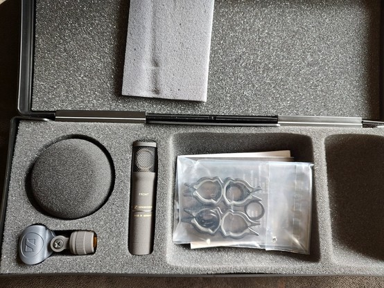 A new Sennheiser MKH 8030 figure 8 microphone in its box with a baggie of clips and foam wind protection. Everything is gray.