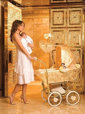 Melania holding Baby Barron in a gaudy golden room with a gaudy golden door pushing a gaudy golden stroller that has it's own mobile chandelier.
