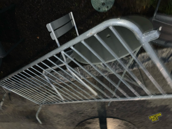 Metal barricade balanced very askew amidst overturned and inter tangled metal tables and chairs