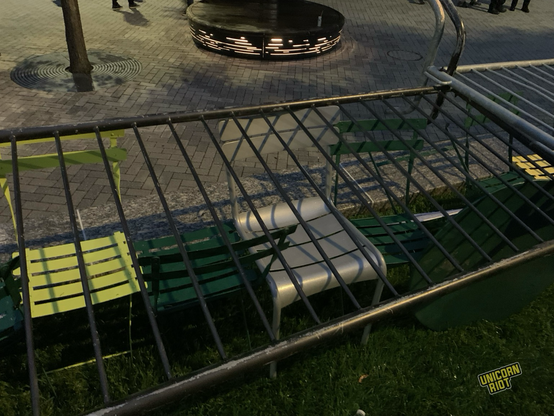 Metal barricades laid over overturned lawn chairs sideways not as intended by police presumably as part of protest barricade. Evening dusk lighting over concrete and dark green grass