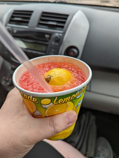 Image shows a cup of cherry lemonade with a straw and half a lemon in it.