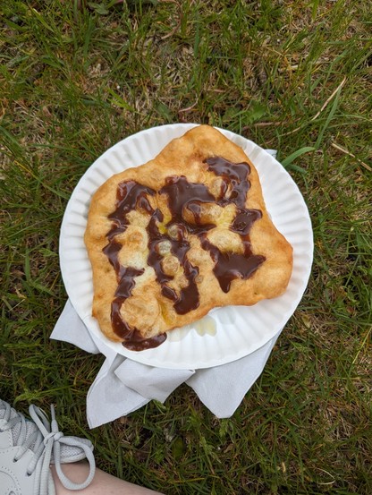 Image shows fried dough on a paper plate. There is chocolate on the fried dough.