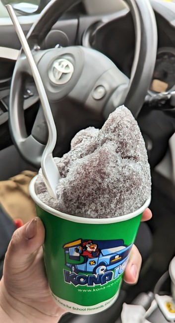 Image shows a cup of grape shaved ice with a spoon in it.