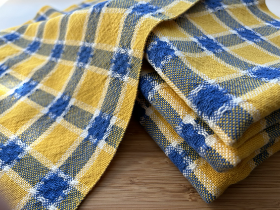 A stack of handwoven yellow, blue and white striped teatowels with huck lace detsils