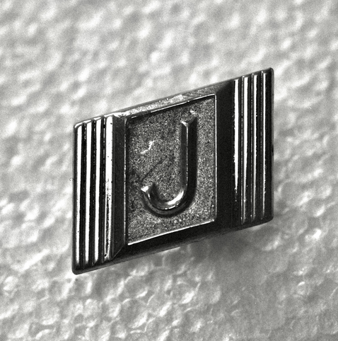 A black and white film photo. A close-up of an old cufflink with the letter J in the center of it. November 2022.