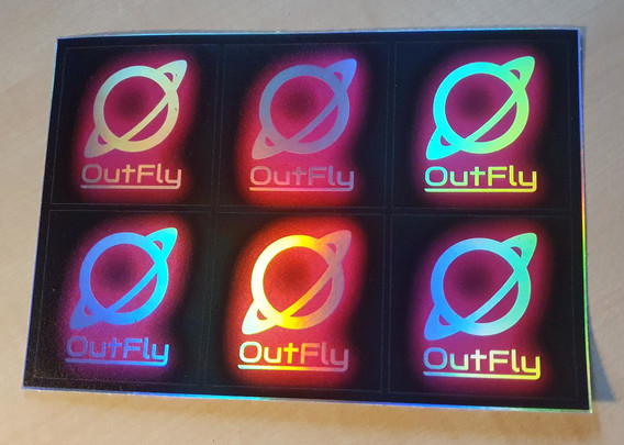 A set of 6 stickers with the outfly logo. What would normally be white, is instead glowing in various colors due to viewing the underlying iridescent silver foil at various angles