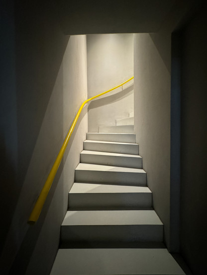Eine schlichte Betontreppe im Brauquadrat Mannheim. Gelbes Rohr als Geländer. Der Clou, der dieses Bild so besonders werden lässt ist das von oben einfallende Licht, der die Treppe und die schmucklosen Betonwände beleuchtet während drumherum alles im Dunkeln liegt.