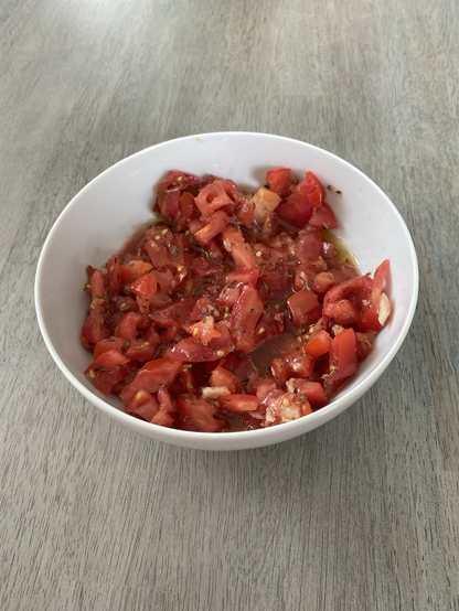 A white bowl with bright red fresh tomatoes smashed with garlic and dill seeds