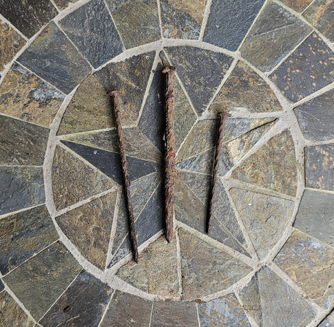 Three large very rusty nails laying on a star made of tile chips shaped into a star with circles around.