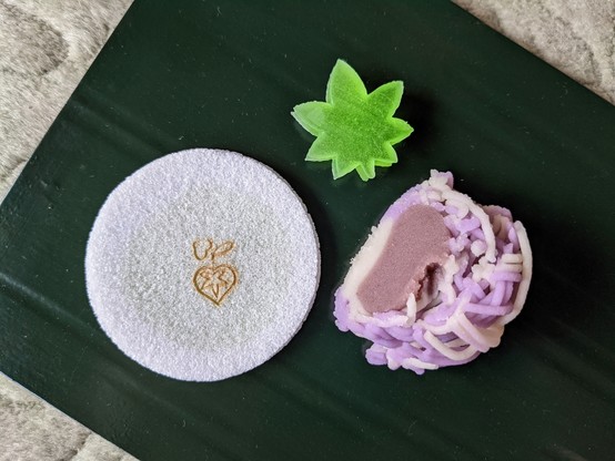 A selection of spring-themed sweets (purple kinton representing a layered kimono, jelly in a maple leaf shape, and wafer depicting a wild ginger leaf).