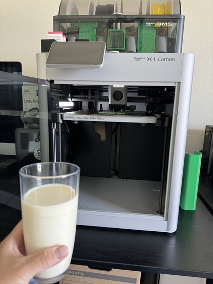 Me holding a glass of soymilk, sitting next to my 3d printer and watching it printing