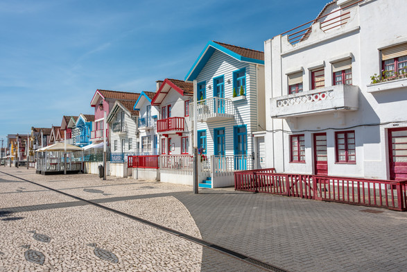 A photograph of a row of houses painted in whites with stripes of bright primary colors along the promenade in Costa Nova do Prado.
