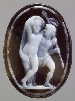Roman onyx cameo depicting the god Bacchus in the nude, his arm slung around his satyr friend. The satyr is wearing a kilt around his looins and holds the god's thyrsos as he gazes adoringly at him. The image is worked in white on a brown background.