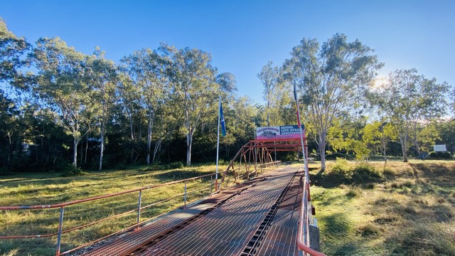 A metal bridge in a grassy, wooded area on a sunny day.