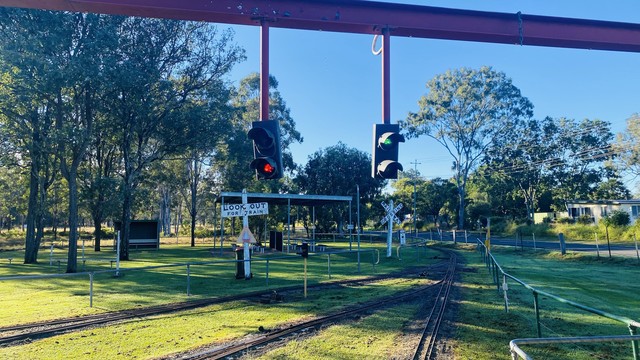 A small rail track at a park with traffic lights, a "LOOK OUT FOR TRAIN" sign, and a "RAILROAD CROSSING" sign.