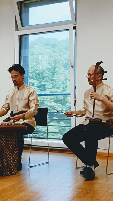 A Khim (Thai hammered dulcimer) player and a Sor Duang (Thai high fiddle) player, both wearing Thai formal shirts.