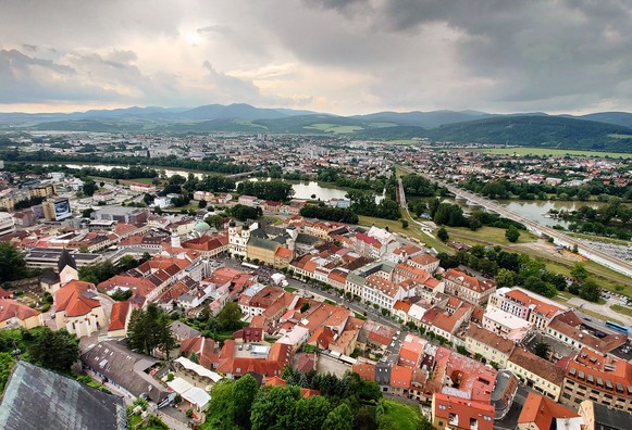 Blick über eine Stadt, es sjnd viele rote Dächer zu sehen und im Hintergrund Berge. 