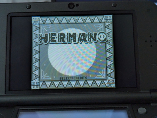A photograph of the top screen of a New Nintendo 3DS XL, running the game "Hermano".  The title screen of the game is displayed.