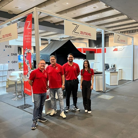 Vier Mitarbeiter*innen stehen an unserem Stand auf der BiblioCON 2024 in Hamburg und warten auf unsere Kunden und Interessenten.