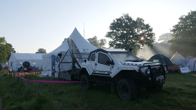 Uplink and downlink dishes pointing at QO-100 with an offroad vehicle in the foreground. Rays of morning sunshine can be seen through the fog