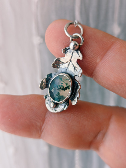 Colgante de plata hoja de roble con piedra ágata musgo ovalada en el centro. La sujeto en mi mano.