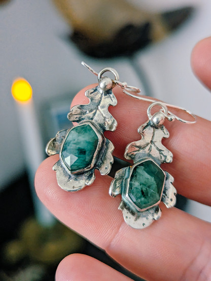 Pendientes hoja de roble con esmeraldas facetadas de apariencia tosca. Los muestro en mi mano.
