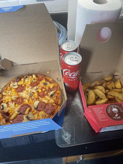 A dominoes pizza with pepperoni, pineapple, mushrooms, and sweetcorn. Two cans of Coca Cola. And a portion of potato wedges. 