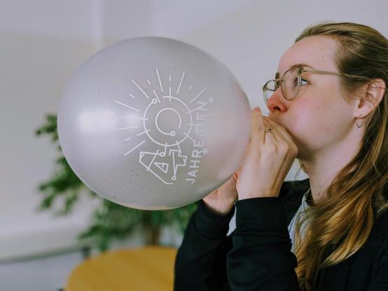 DFN-Mitarbeiterin bläst silbernen Luftballon mit weißem 40-Jahre-DFN-Logo auf.