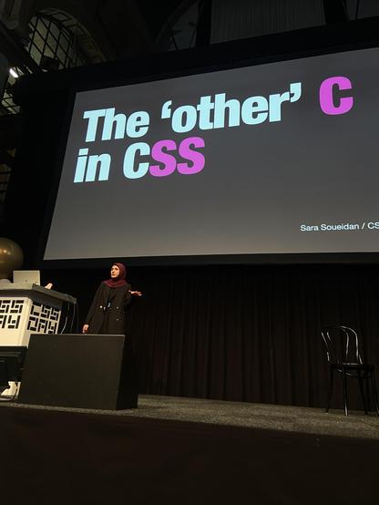 Sara on stage with the title slide: The “other” C in CSS