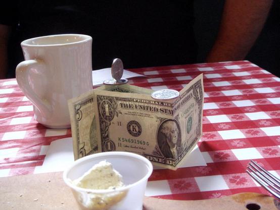 patron economy impact events: photograph of a cafe table with a red and white checked tablecloth, a coffee mug, fork, napkins, and a tip. Photo attribution: Flickr user cali2okie