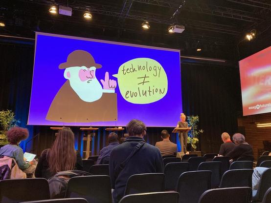 me in front of a projection of an illustration of darwing saying tech is not evolution